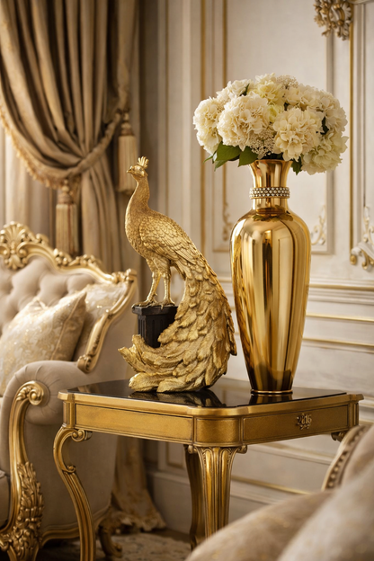 Royal Gold Peacock Figurine lifestyle — gold sculptural peacock on black marble side table beside tall gold vase with white hydrangeas in luxurious gold and cream French-style living room