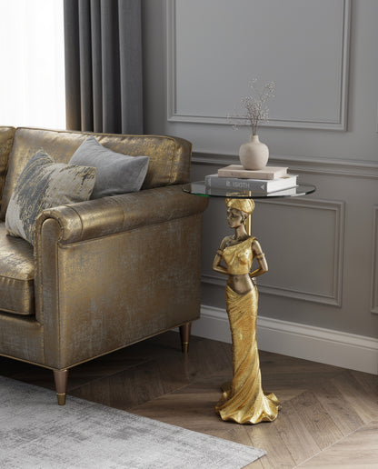 Gold African Queen Sculptural Glass Side Table lifestyle — 41 inch gold draped queen pedestal table with stacked books and small bud vase on glass top beside gold Chesterfield sofa in grey and gold panelled living room
