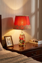 Crimson Rose Table Lamp lifestyle — deep crimson jewel-tone glow illuminating dark wood bedroom nightstand beside framed photograph and stacked books with warm romantic ambient light on walls
