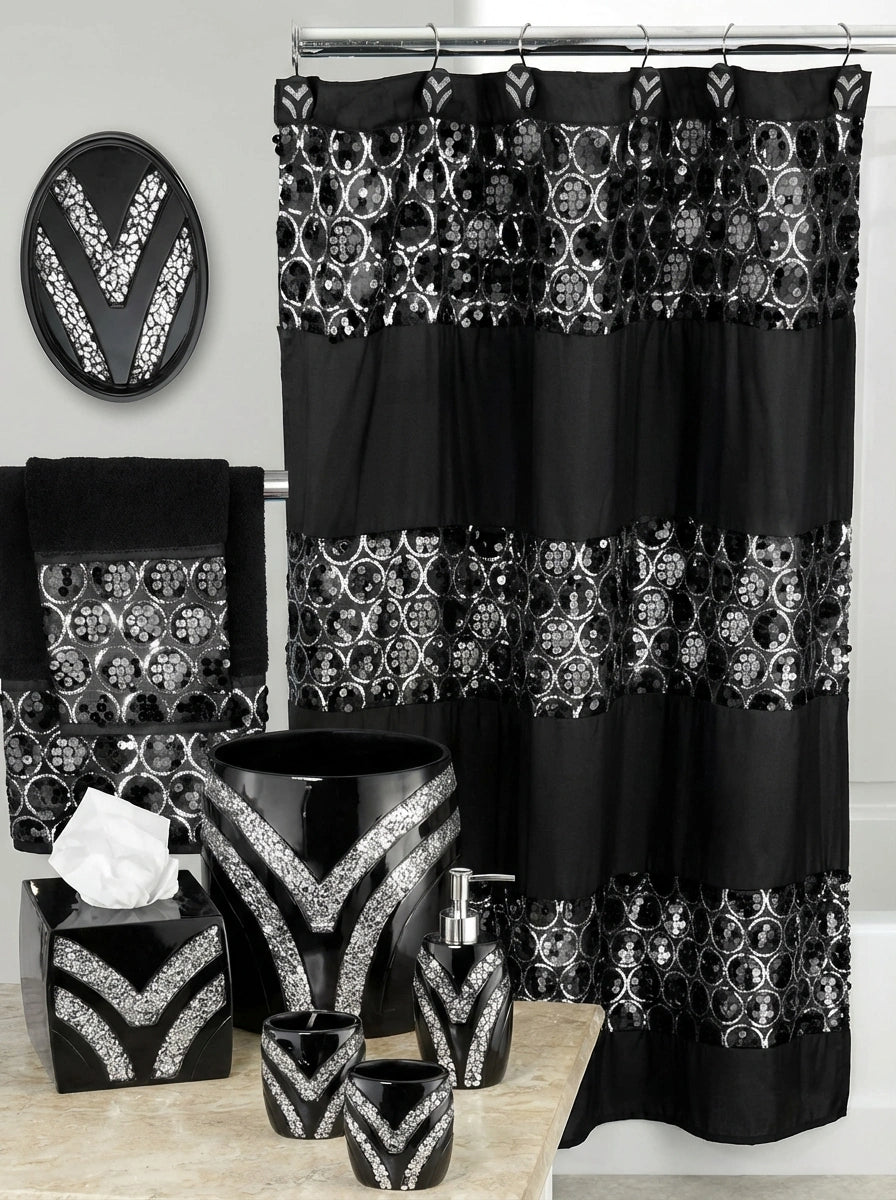 Sinatra Black accessories lifestyle — V-chevron mosaic black resin accessories on white marble vanity counter beside silver ornate mirror, stacked white towels and white hydrangeas under crystal sconce