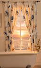 Spa Shell window curtain — coastal seashell and starfish print panel with tie-back, framing ocean sunset view over clawfoot tub